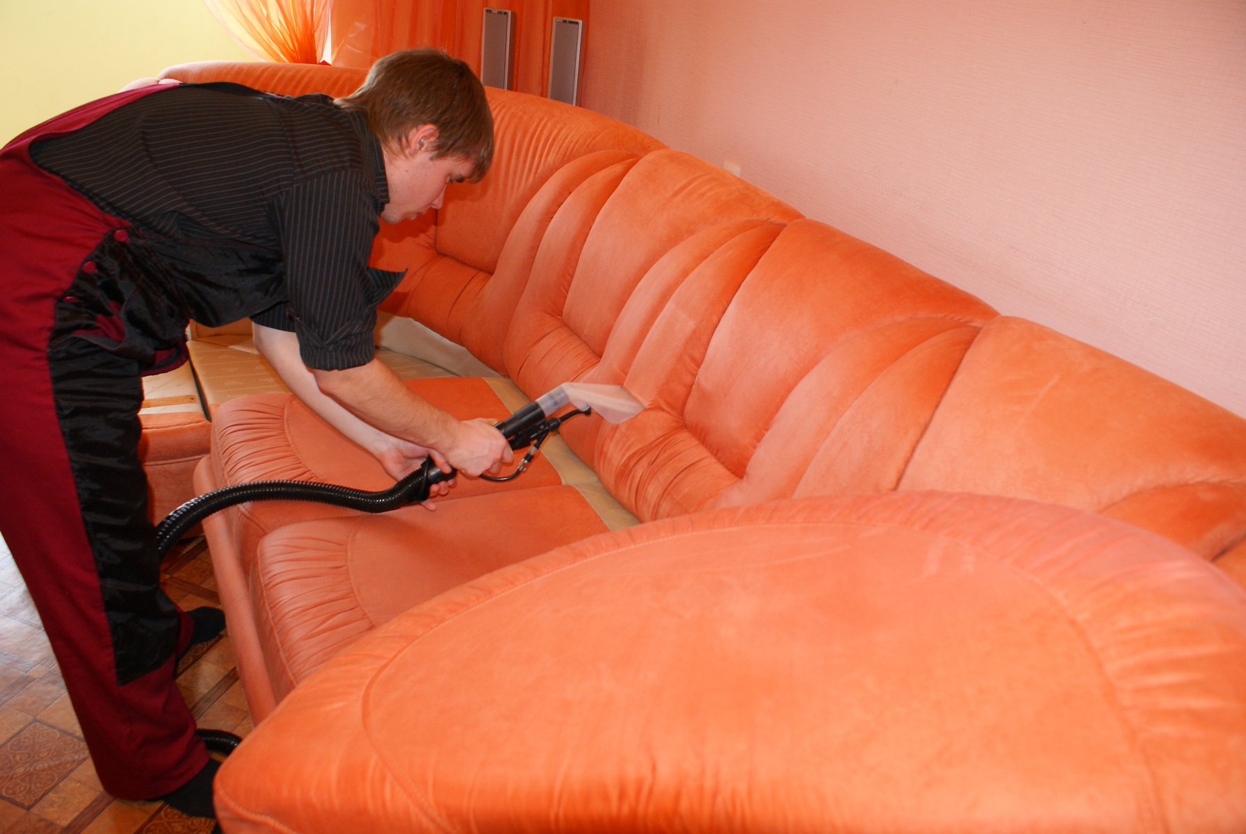 Мастер производит чистку кожаного дивана с помощью пылесоса